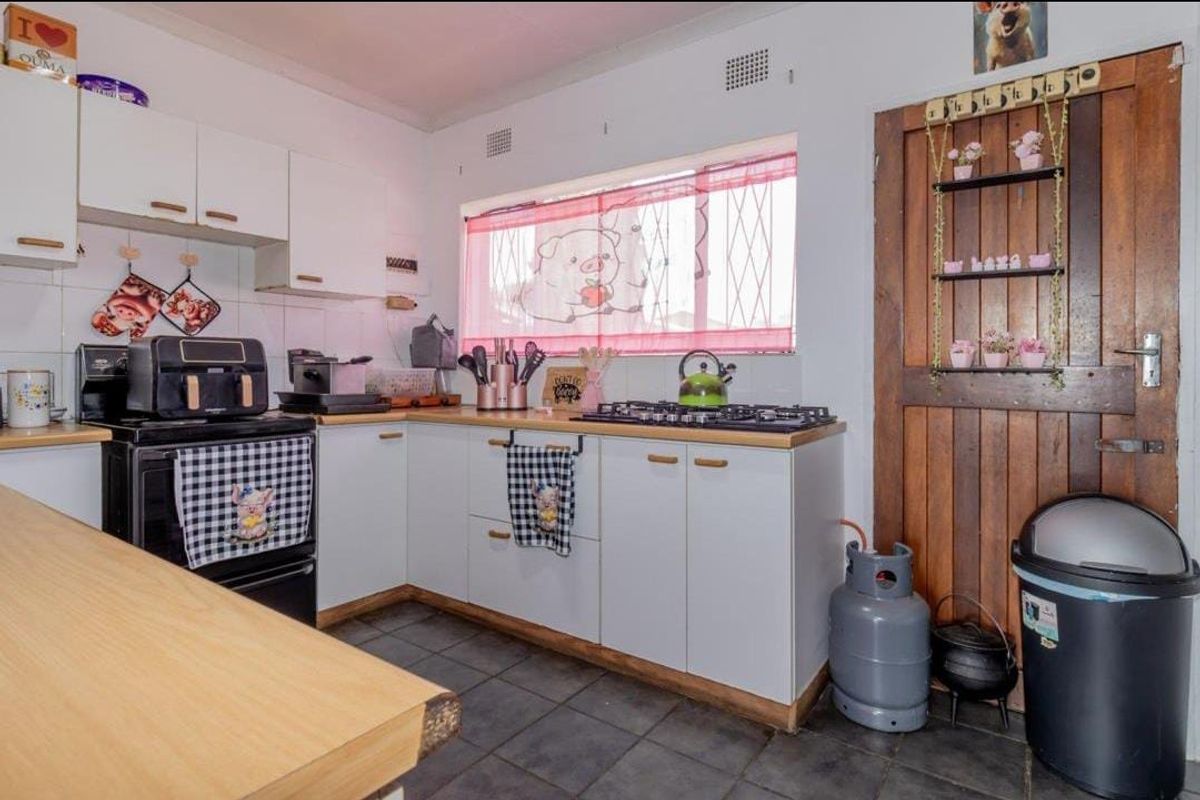 A functional kitchen featuring white cabinetry, a gas hob, freestanding oven, and tiled flooring, with a rustic timber door and security-barred window.