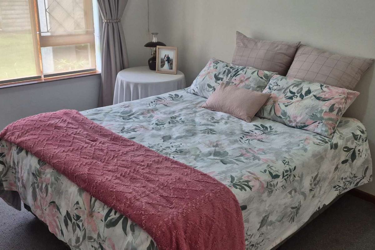 A well-lit bedroom featuring neutral walls, carpeted flooring, and a large window allowing for natural light.