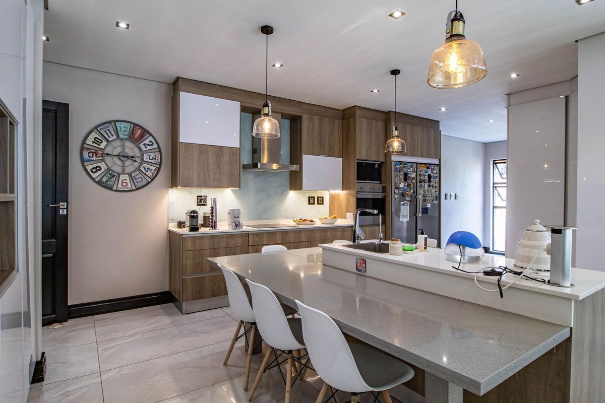 Modern kitchen featuring wood-grain cabinetry, stone countertops, a central island with breakfast bar seating, and integrated stainless steel appliances.