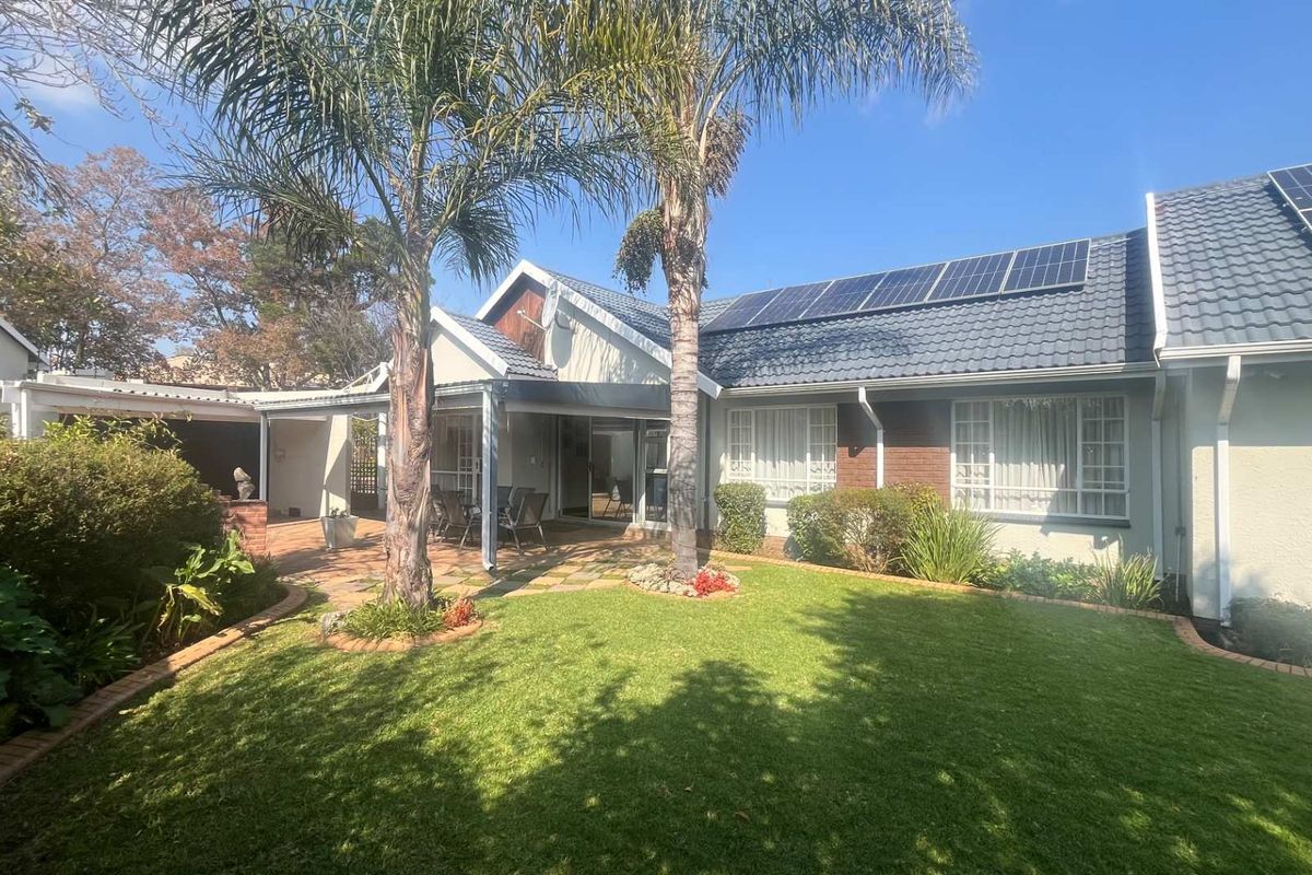 Rear view of the house featuring a landscaped garden, paved patio area, and roof-mounted solar panels.
