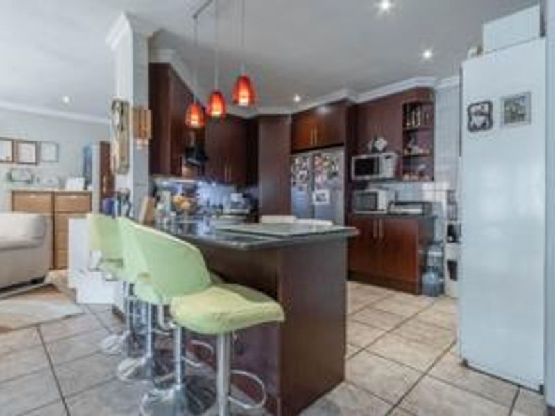 Open-plan kitchen featuring dark wood cabinetry, granite countertops, and integrated appliances, seamlessly flowing into the adjacent living area with tiled flooring throughout.