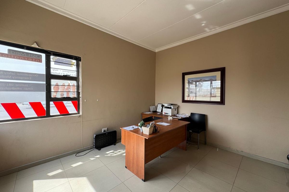 A functional office space featuring tiled flooring, neutral wall finishes, and a large window with exterior signage.