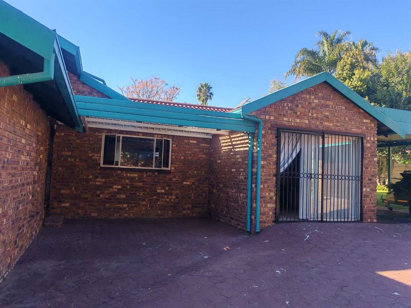 Rear exterior view of the house featuring face brick walls, a paved patio area, and a metal security gate over the sliding door entrance.
