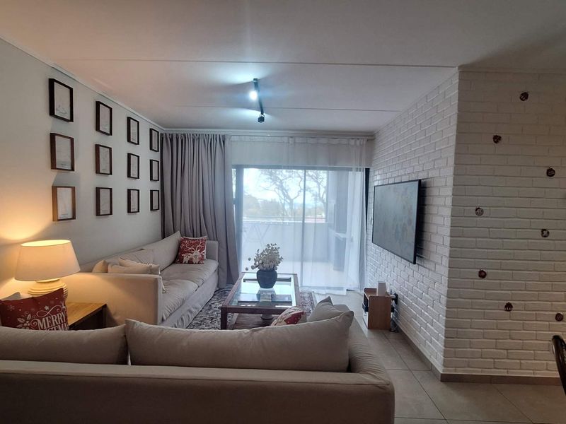 A well-maintained living room featuring an exposed white brick feature wall, tiled flooring, and direct access to a balcony through sliding glass doors.