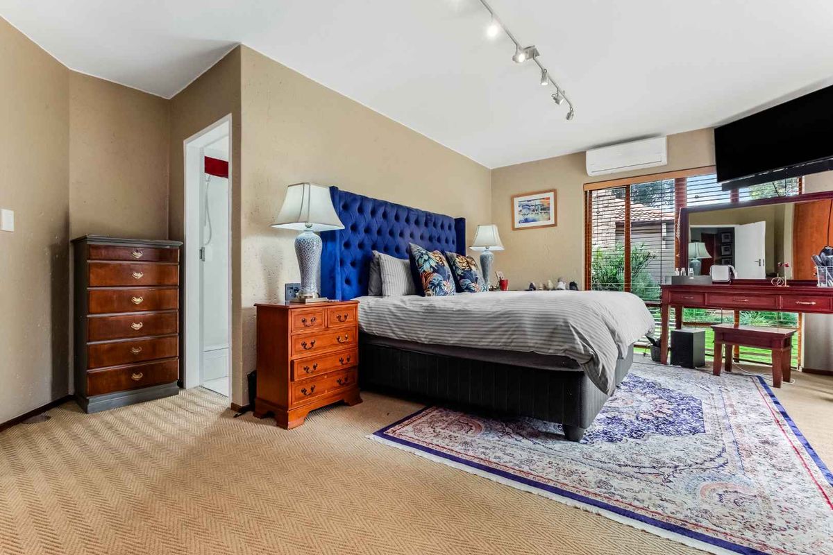 Spacious bedroom featuring neutral carpeting, a wall-mounted air conditioning unit, and direct access to an en-suite bathroom.