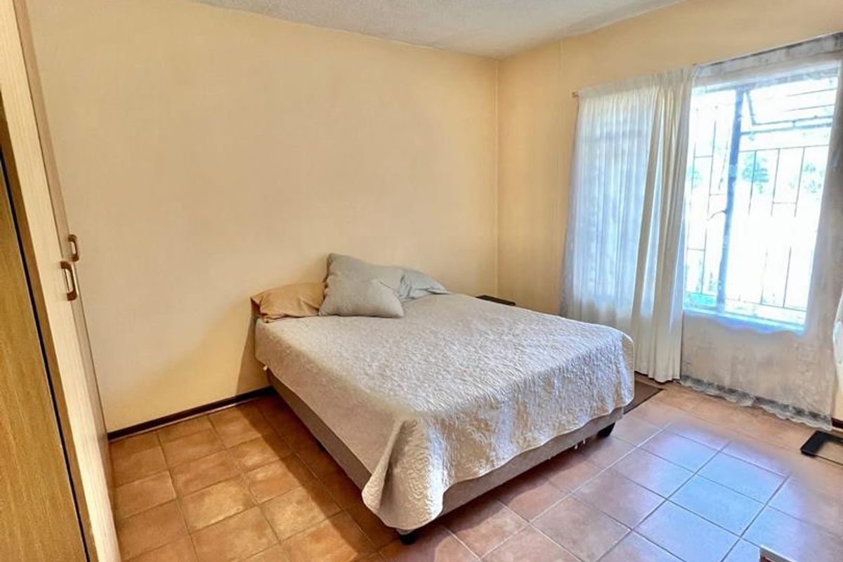 A bedroom featuring tiled flooring, built-in cabinetry, and a window with security bars, providing a functional and well-lit living space.