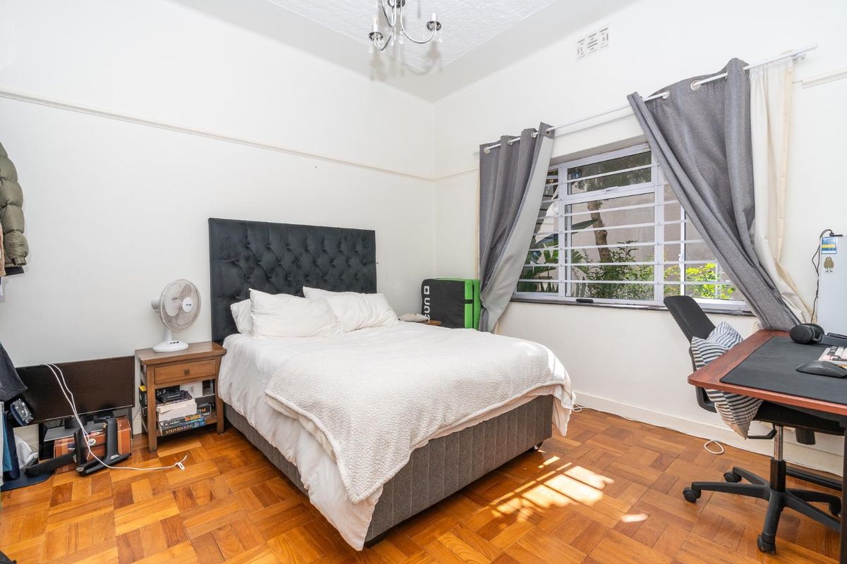 A bedroom featuring classic parquet flooring, high ceilings with picture rails, and a window fitted with security bars.