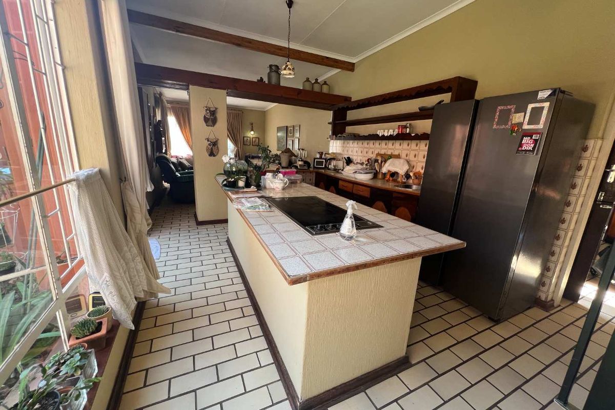 A spacious kitchen featuring a central island with a built-in cooktop, tiled countertops, and open shelving, flowing into an adjacent living area.