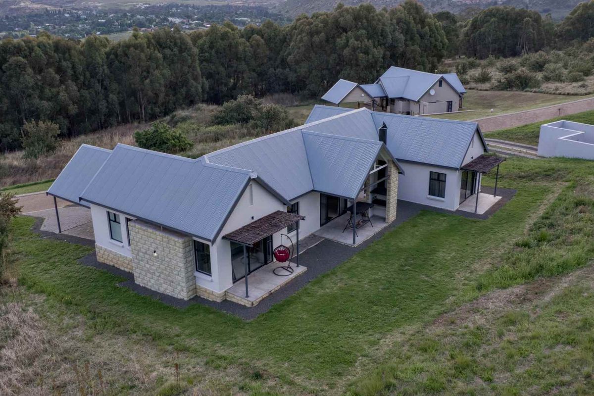 Aerial view of a modern farmhouse-style residence featuring a corrugated metal roof, stone cladding accents, and covered patio areas set in a rural landscape.