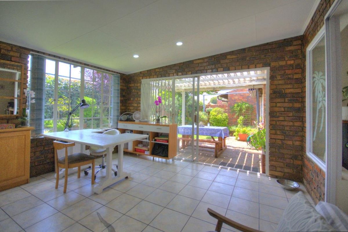 A sun-filled living area featuring exposed brick walls, tiled flooring, and large sliding glass doors that open onto a covered patio and garden.