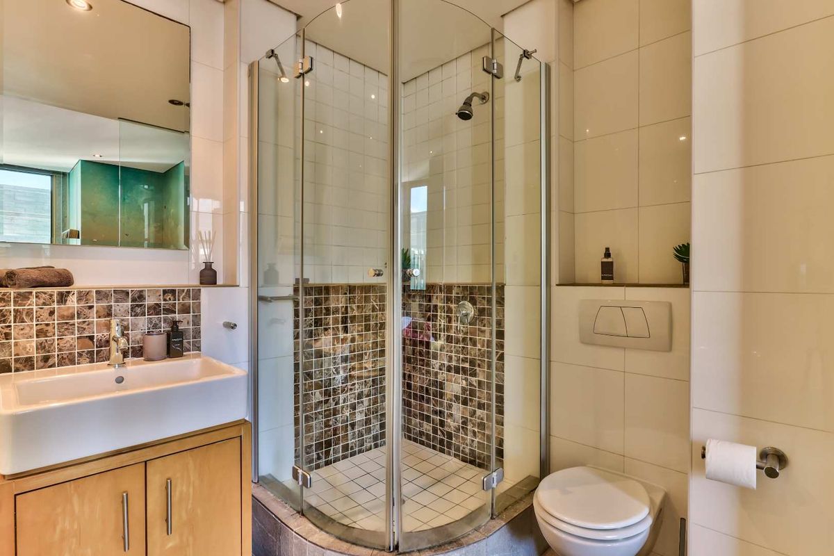 Modern bathroom featuring a wall-mounted vanity with vessel sink, a corner glass shower enclosure, and a wall-hung toilet with mosaic tile accents.