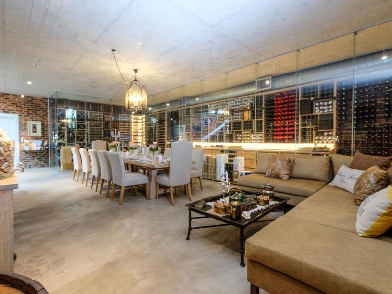 A sophisticated, climate-controlled wine cellar featuring extensive glass-enclosed racking, exposed brickwork, and a polished concrete floor, integrated with a dining and lounge area.
