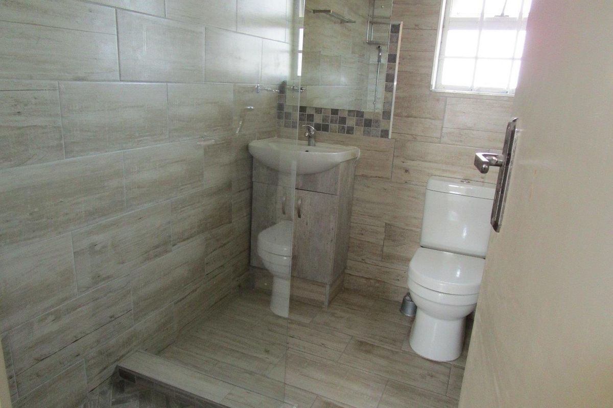 A modern bathroom featuring a walk-in shower with glass screen, vanity basin, and toilet, finished with neutral wood-look wall and floor tiles.