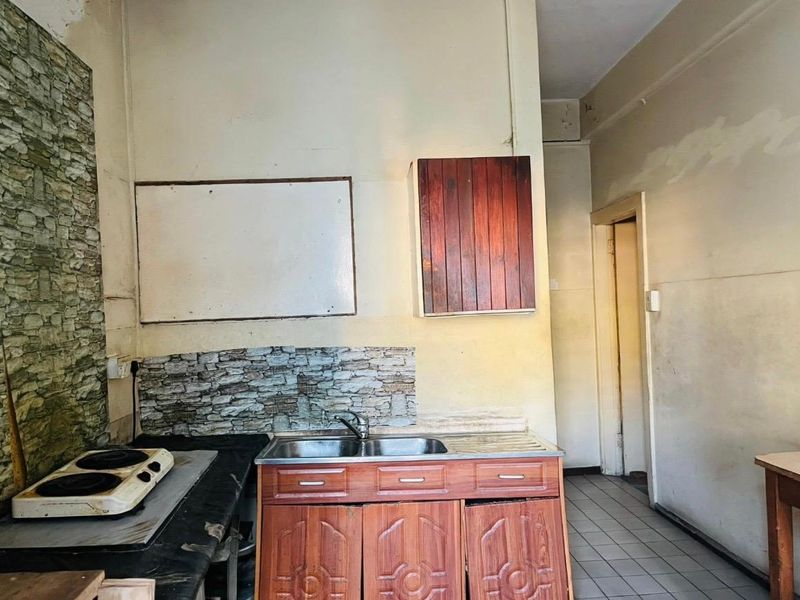 A dated kitchen area featuring built-in wooden cabinetry, a stainless steel sink, and an electric hob, requiring cosmetic updates and wall repairs.