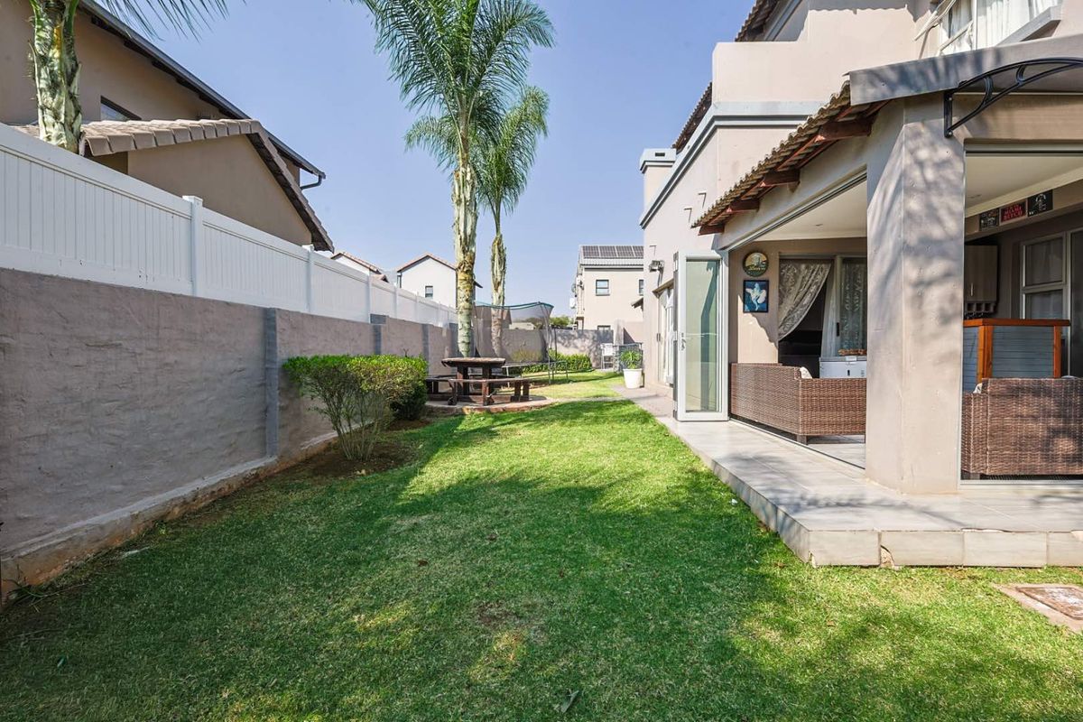 A well-maintained rear garden featuring a covered patio area, lawn, and boundary wall with vinyl fencing, providing a private outdoor space.