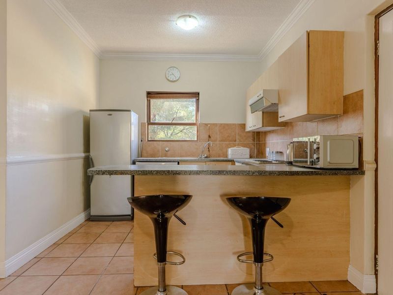 A functional kitchen featuring light wood cabinetry, tiled backsplash, a breakfast bar, and tiled flooring, offering a practical layout for daily use.