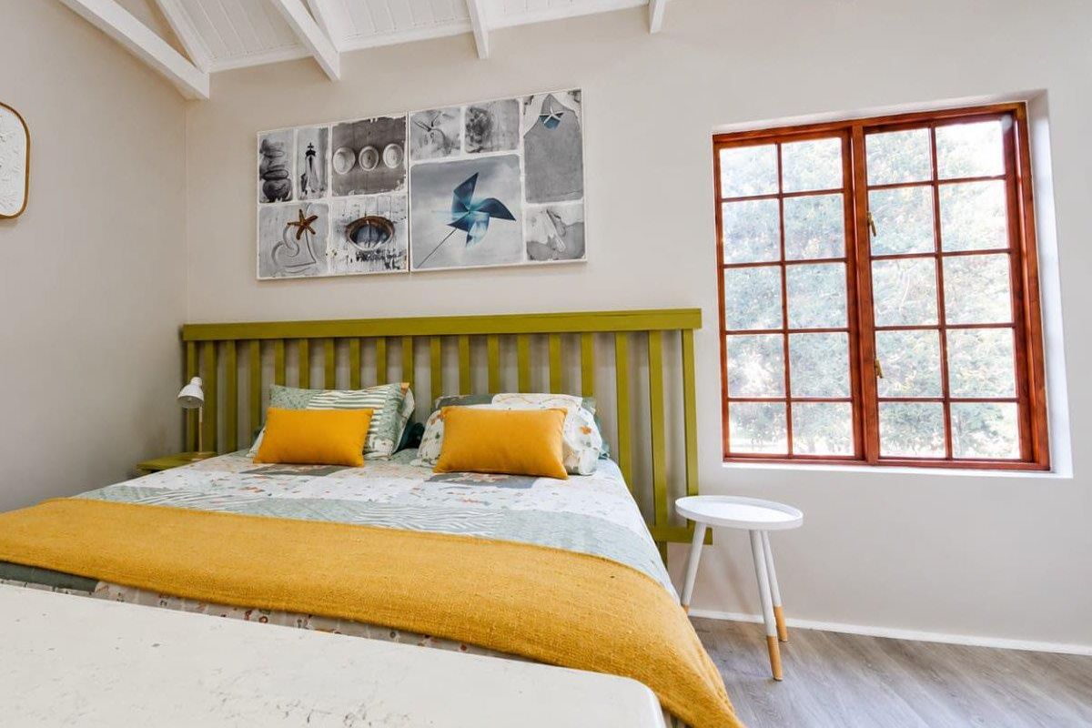 A bright bedroom featuring exposed timber ceiling beams, light-toned flooring, and a large timber-framed window allowing for natural light.
