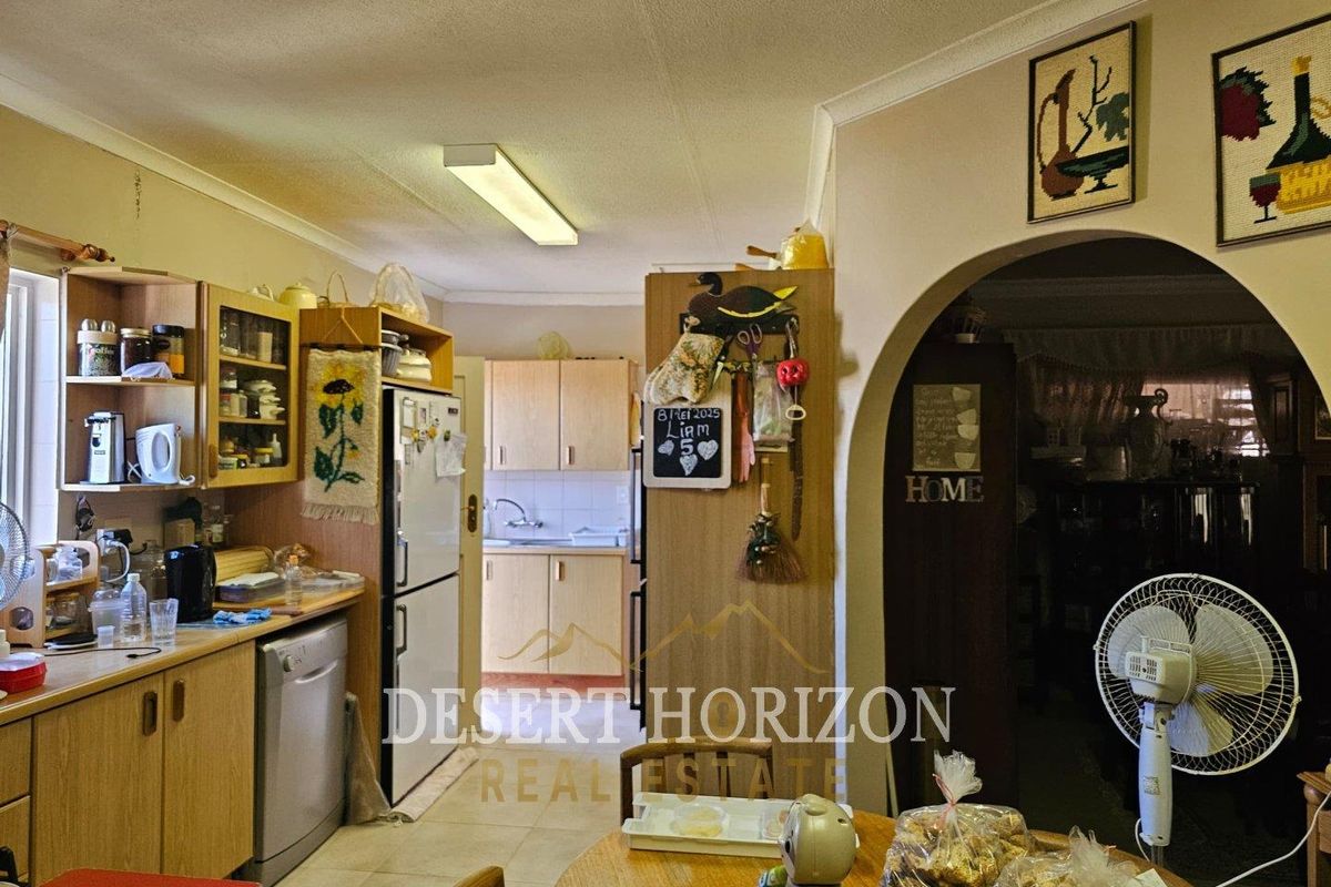 A functional kitchen featuring wood-look cabinetry, laminate countertops, and an arched entryway leading to the adjacent living space.