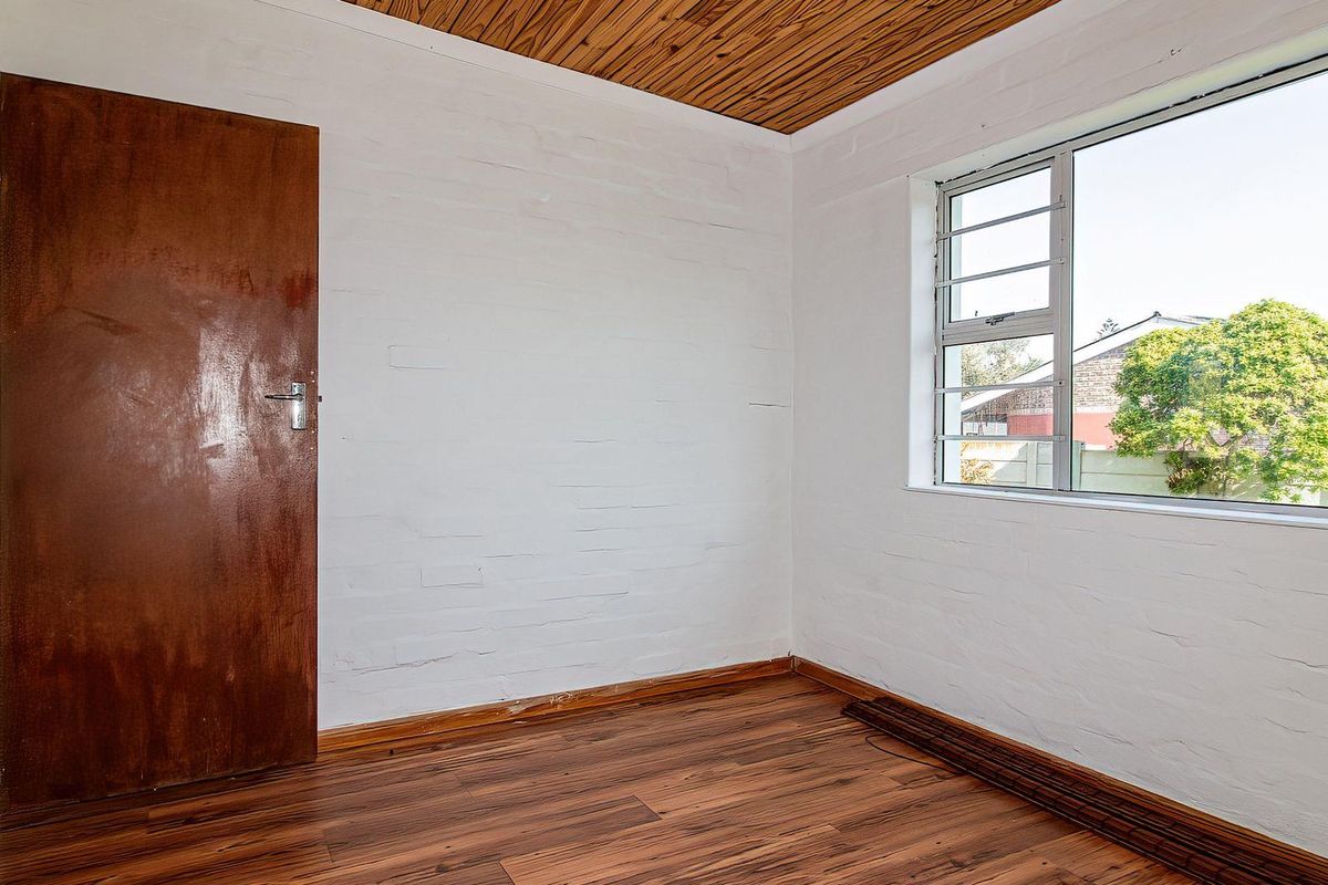 An empty bedroom featuring laminate flooring, a timber ceiling, and a window with security bars.