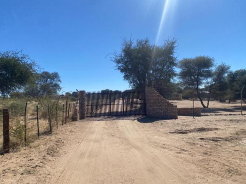 A secure entrance to the small holding featuring a metal gate flanked by stone masonry pillars and wire perimeter fencing along a dirt driveway.