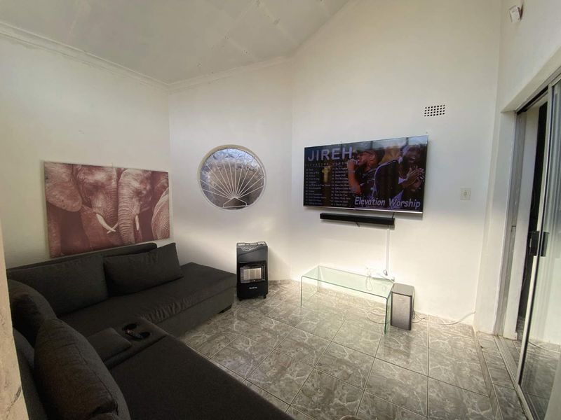 A living room featuring tiled flooring, a unique porthole window, and a wall-mounted television, with visible ceiling maintenance required.