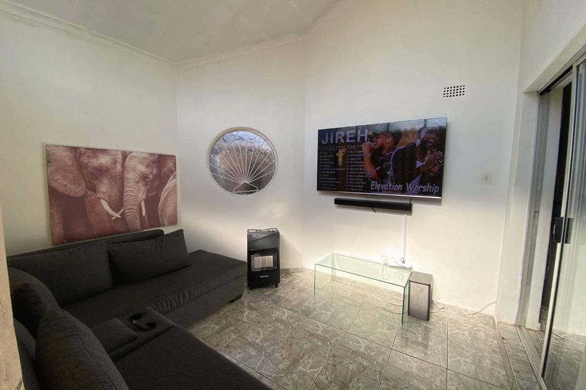 A living room featuring tiled flooring, a unique porthole window, and a wall-mounted television, with visible ceiling maintenance required.