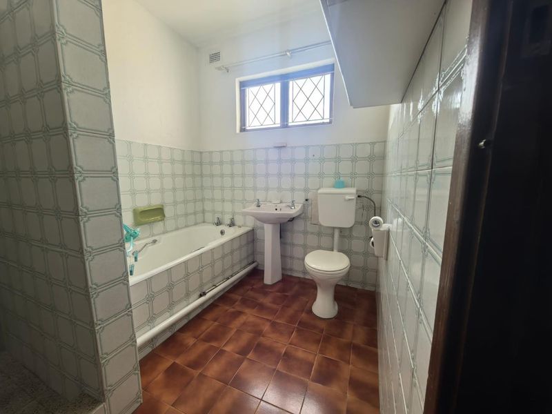 A dated bathroom featuring a standard bathtub, pedestal sink, and toilet with original ceramic wall and floor tiling.