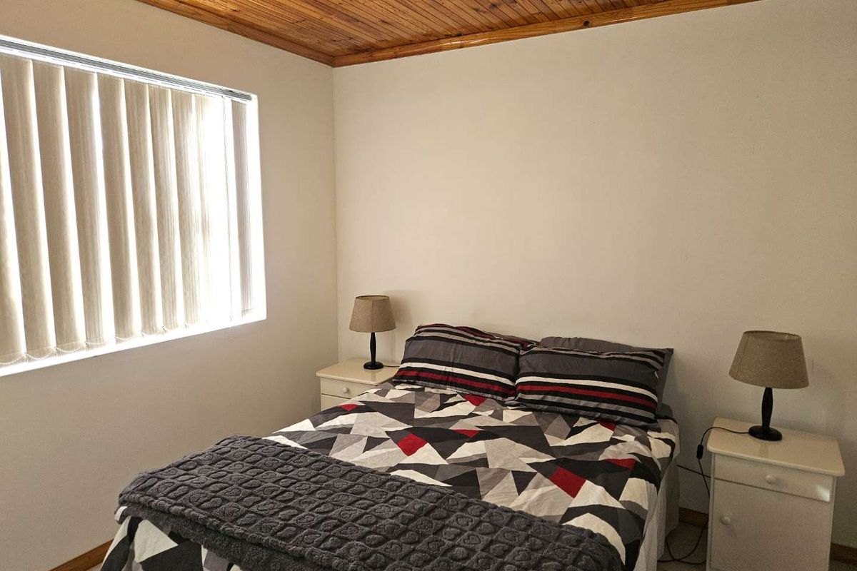 A bedroom featuring a timber-paneled ceiling and vertical window blinds, providing a functional and neutral space.