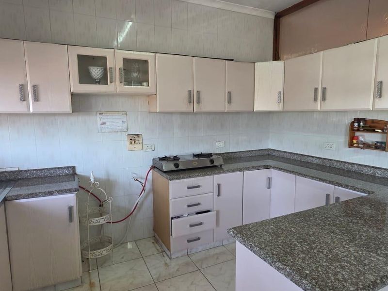 A functional kitchen featuring granite countertops, ample built-in cabinetry, a double stainless steel sink, and a gas hob with tiled splashback.