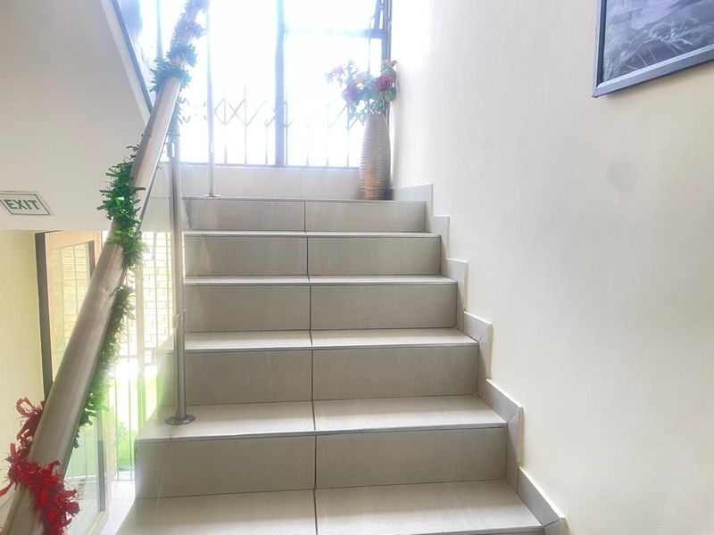 A bright, tiled staircase featuring a modern stainless steel handrail and a secure metal gate at the landing.