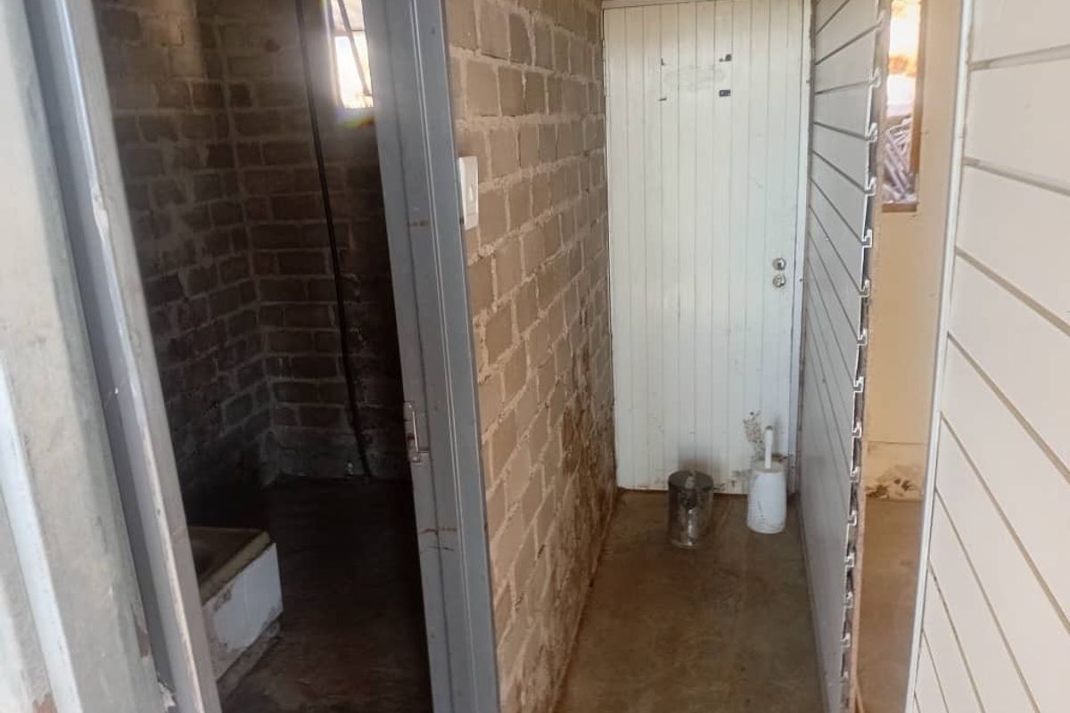A basic, unfinished bathroom area featuring exposed brickwork, concrete flooring, and timber wall paneling, requiring significant renovation and finishing.