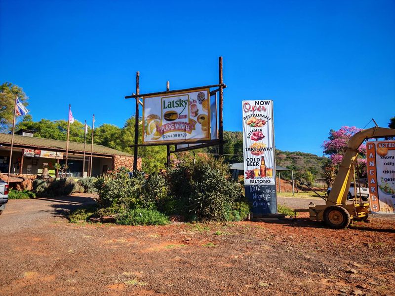 Front view of a mixed-use property featuring prominent signage, a gravel driveway, and established garden landscaping.