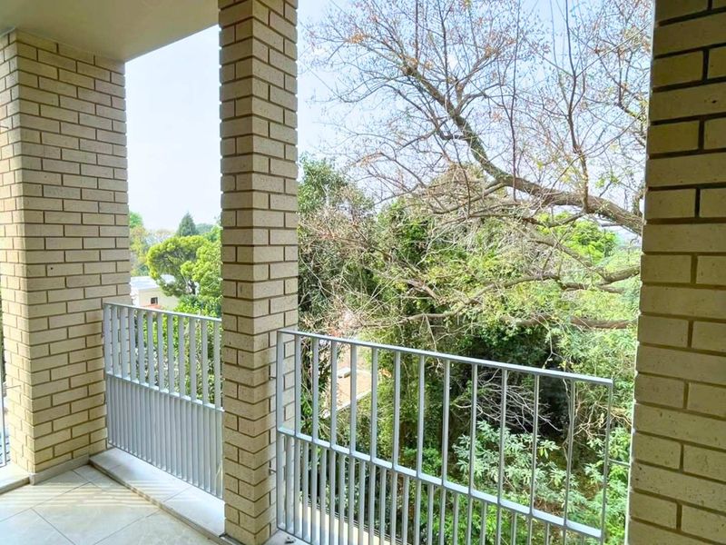 A covered balcony featuring brick columns, a metal balustrade, and tiled flooring, offering an elevated view of the surrounding trees.