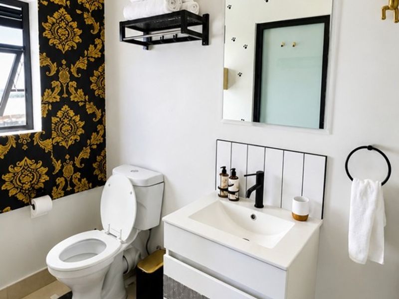 A modern bathroom featuring a wall-mounted vanity with a black mixer tap, a toilet, and decorative wallpaper accents.