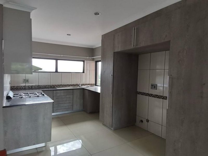 Modern kitchen featuring grey built-in cabinetry, a gas hob, tiled backsplash, and ample space for a refrigerator, finished with neutral floor tiles.