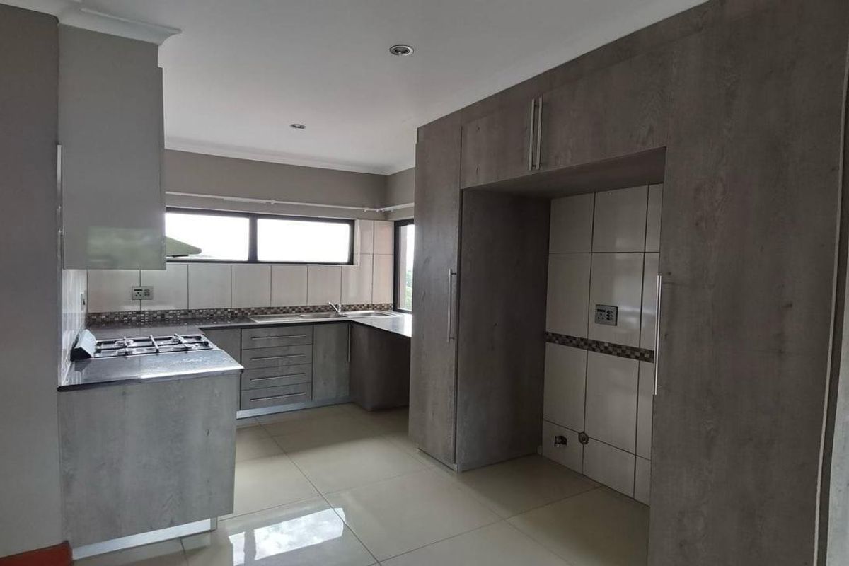 Modern kitchen featuring grey built-in cabinetry, a gas hob, tiled backsplash, and ample space for a refrigerator, finished with neutral floor tiles.