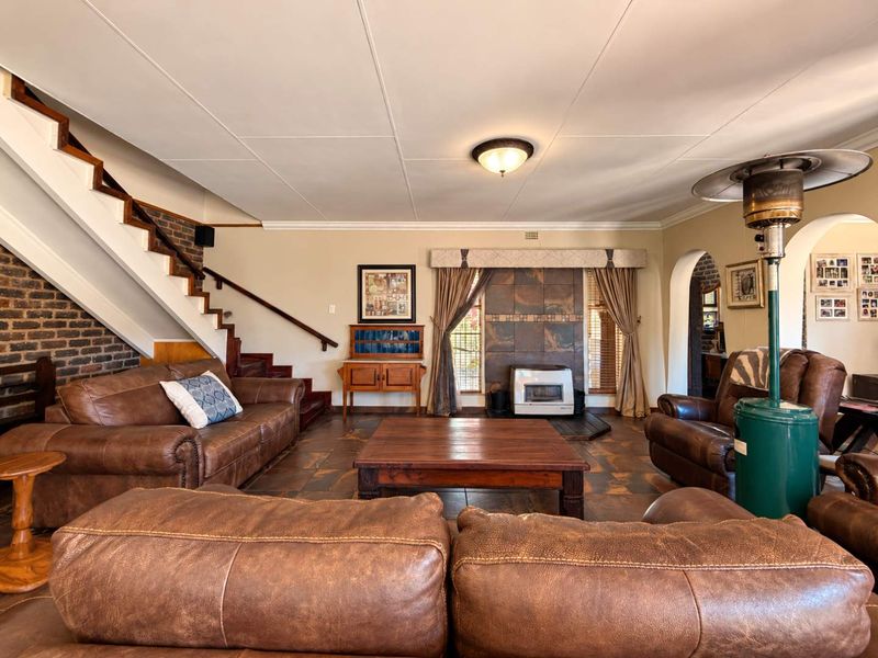 Spacious living room featuring an exposed brick staircase, tiled flooring, and a built-in fireplace, offering a warm and traditional atmosphere.