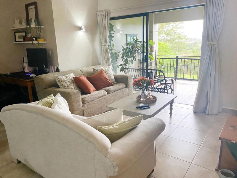 A bright living room featuring tiled flooring and large sliding glass doors that provide seamless access to an outdoor balcony area.