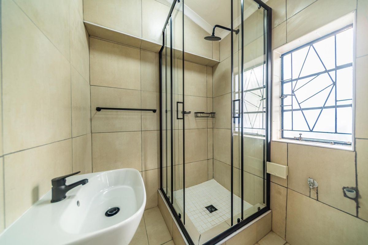A modern bathroom featuring a glass-enclosed shower with a rain shower head, a contemporary basin with a black mixer tap, and neutral wall tiling.