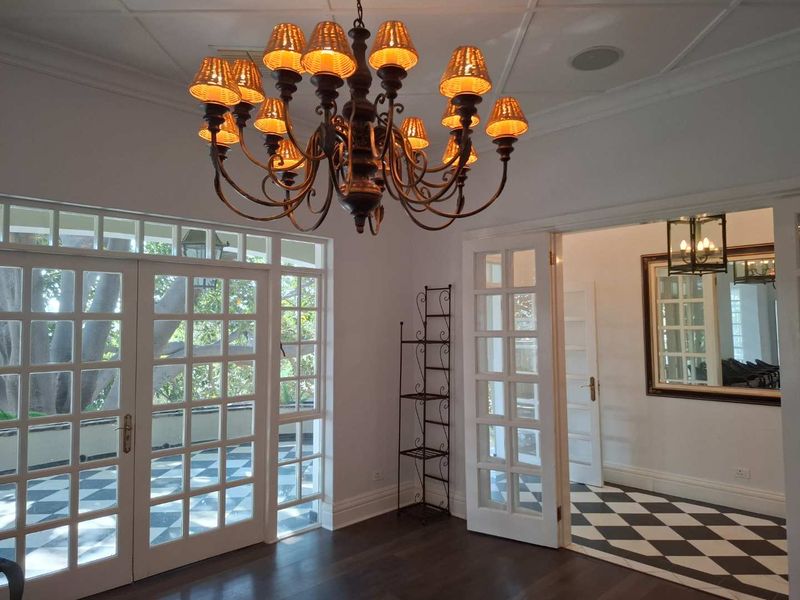 Bright living area featuring elegant hardwood floors, classic french doors opening to a patio, and a sophisticated chandelier, leading into a tiled hallway.
