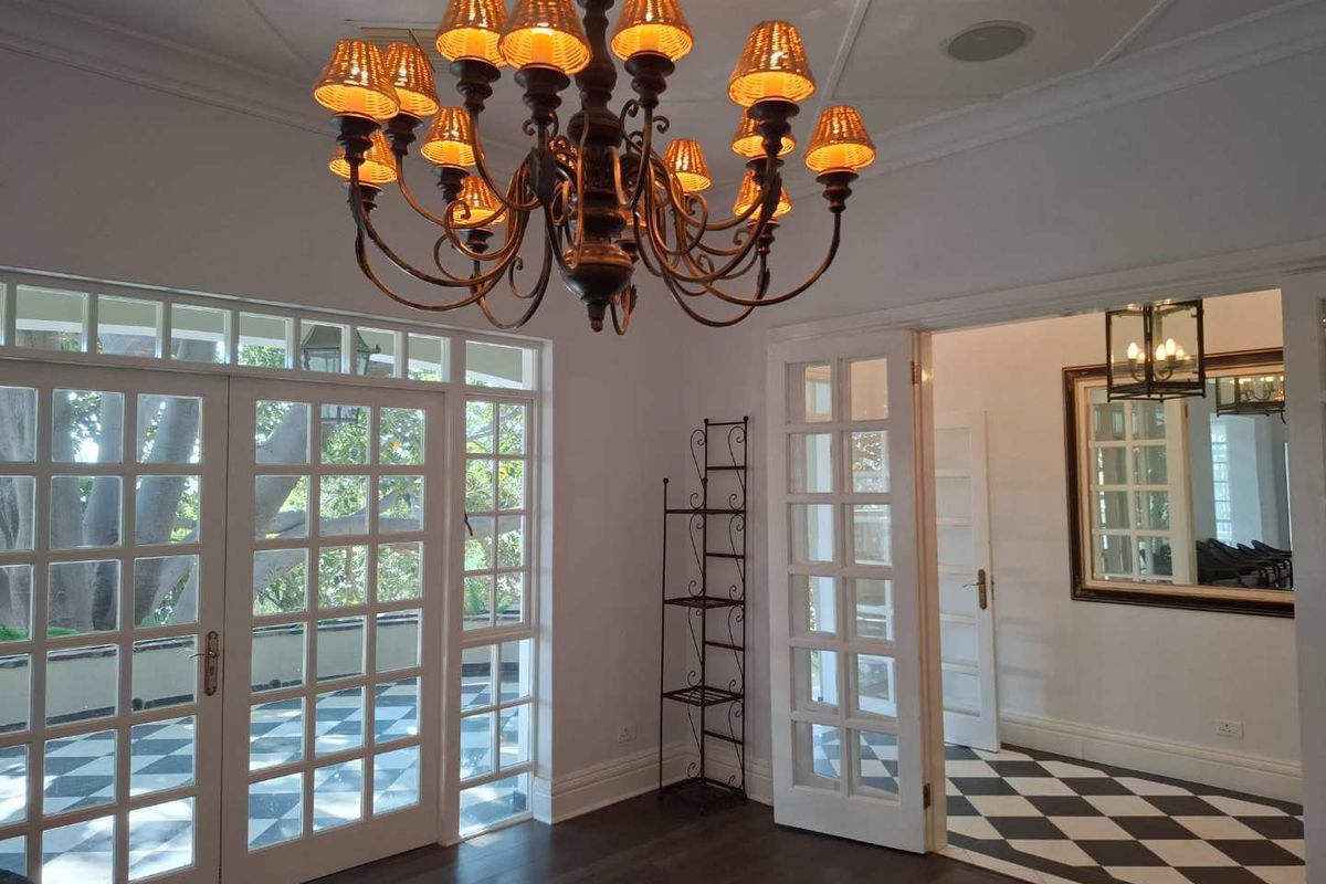Bright living area featuring elegant hardwood floors, classic french doors opening to a patio, and a sophisticated chandelier, leading into a tiled hallway.