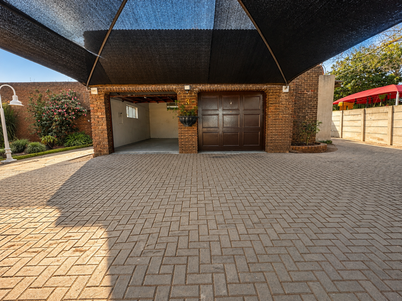 A double garage featuring a brick facade, paved driveway, and a protective shade sail covering the entrance area.