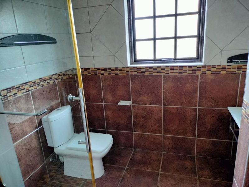 A functional bathroom featuring tiled walls and flooring, a glass shower screen, and a window for natural light.