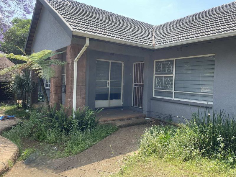 Front elevation of a house featuring stone-clad pillars, security gates, and a tiled roof, set within a garden with a paved walkway.