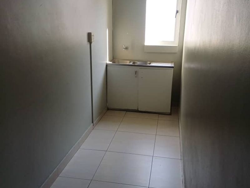 A compact kitchenette area featuring a stainless steel sink, base cabinetry, and tiled flooring, suitable for office utility use.