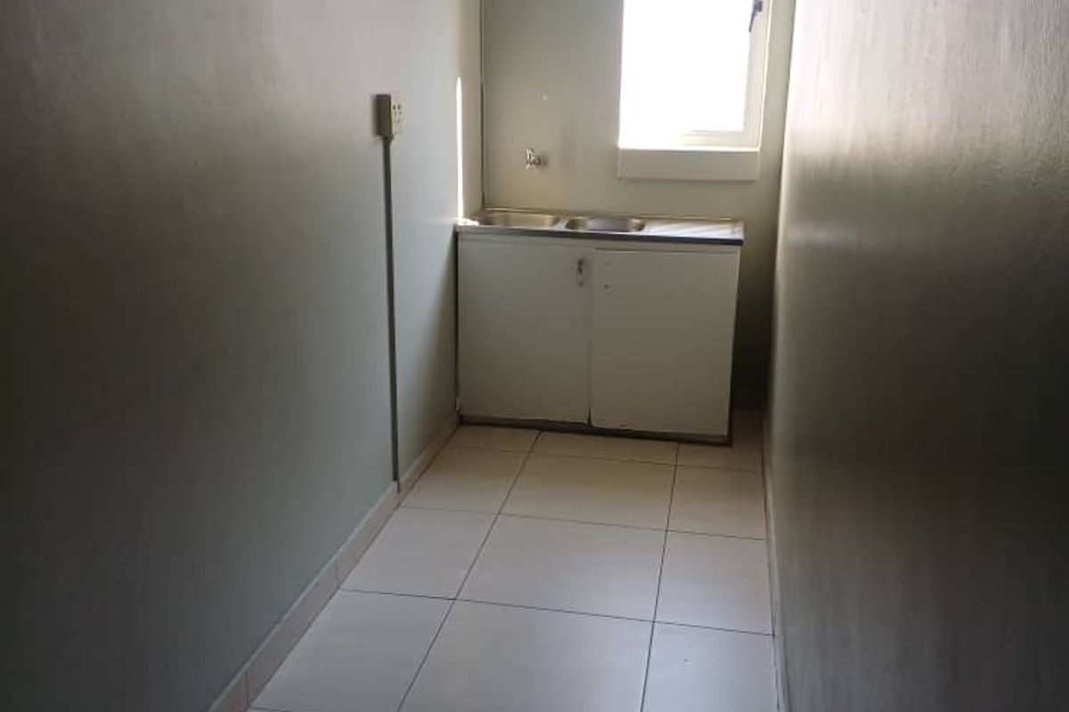 A compact kitchenette area featuring a stainless steel sink, base cabinetry, and tiled flooring, suitable for office utility use.
