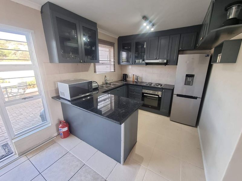 A functional kitchen featuring dark grey cabinetry, granite countertops, built-in oven, electric hob, and tiled flooring with direct access to the patio.
