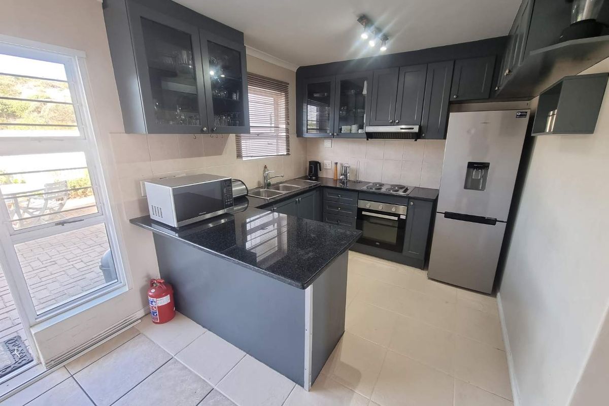 A functional kitchen featuring dark grey cabinetry, granite countertops, built-in oven, electric hob, and tiled flooring with direct access to the patio.