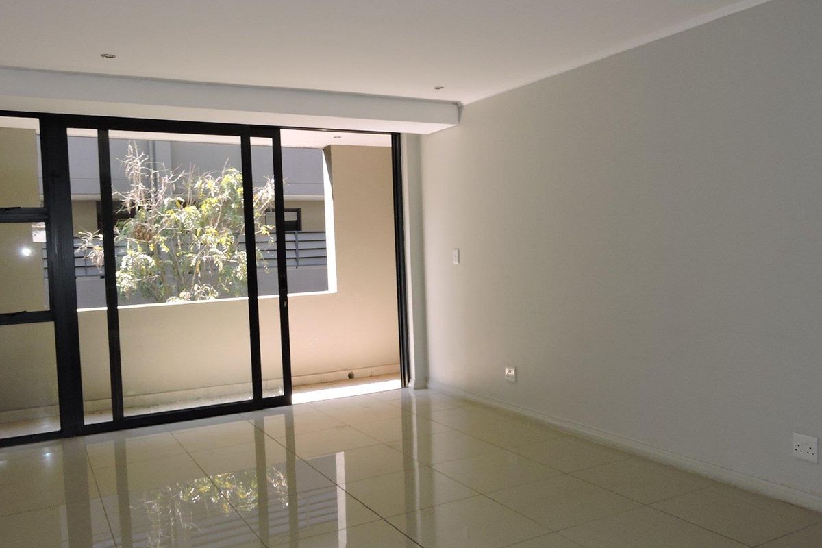 A bright, empty living room featuring polished tiled flooring and large sliding glass doors that open onto a private balcony.