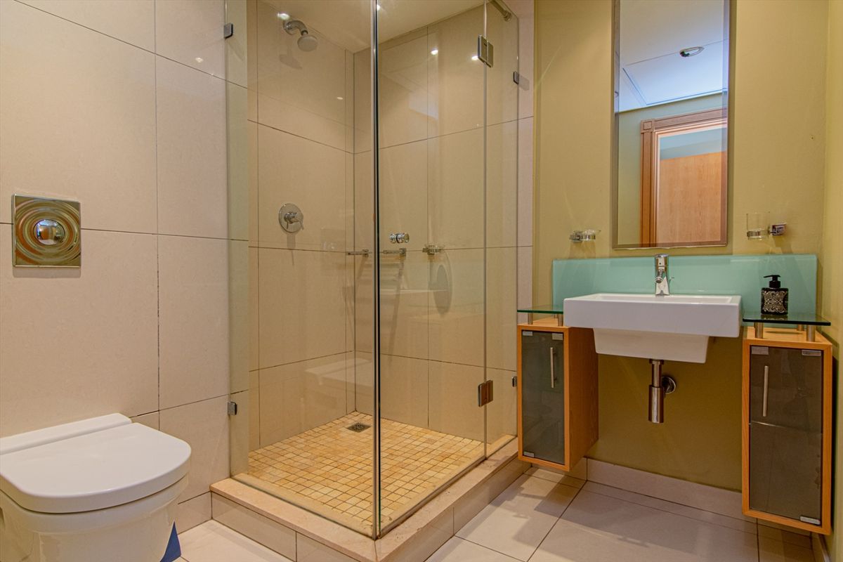 Modern bathroom featuring a glass-enclosed shower, wall-mounted vanity with basin, and tiled flooring.